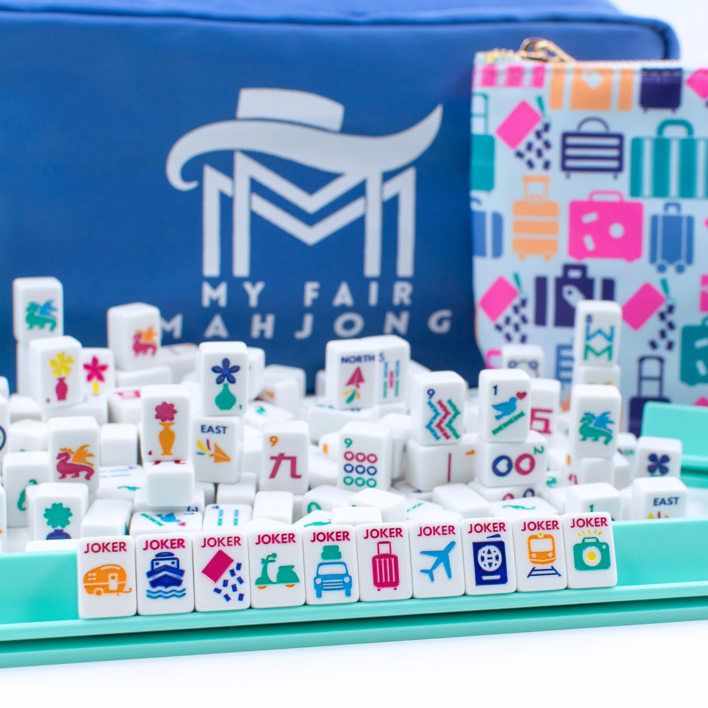 White Go Anywhere mini mahjong set with jokers on a teal mini rack, carry-all box and luggage-pattern grab bag